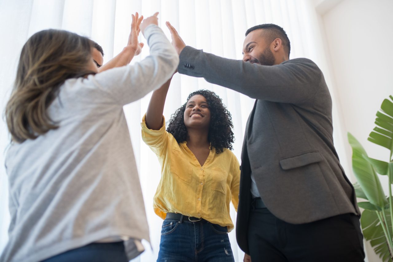 A diverse group of colleagues sharing a high five in a bright office