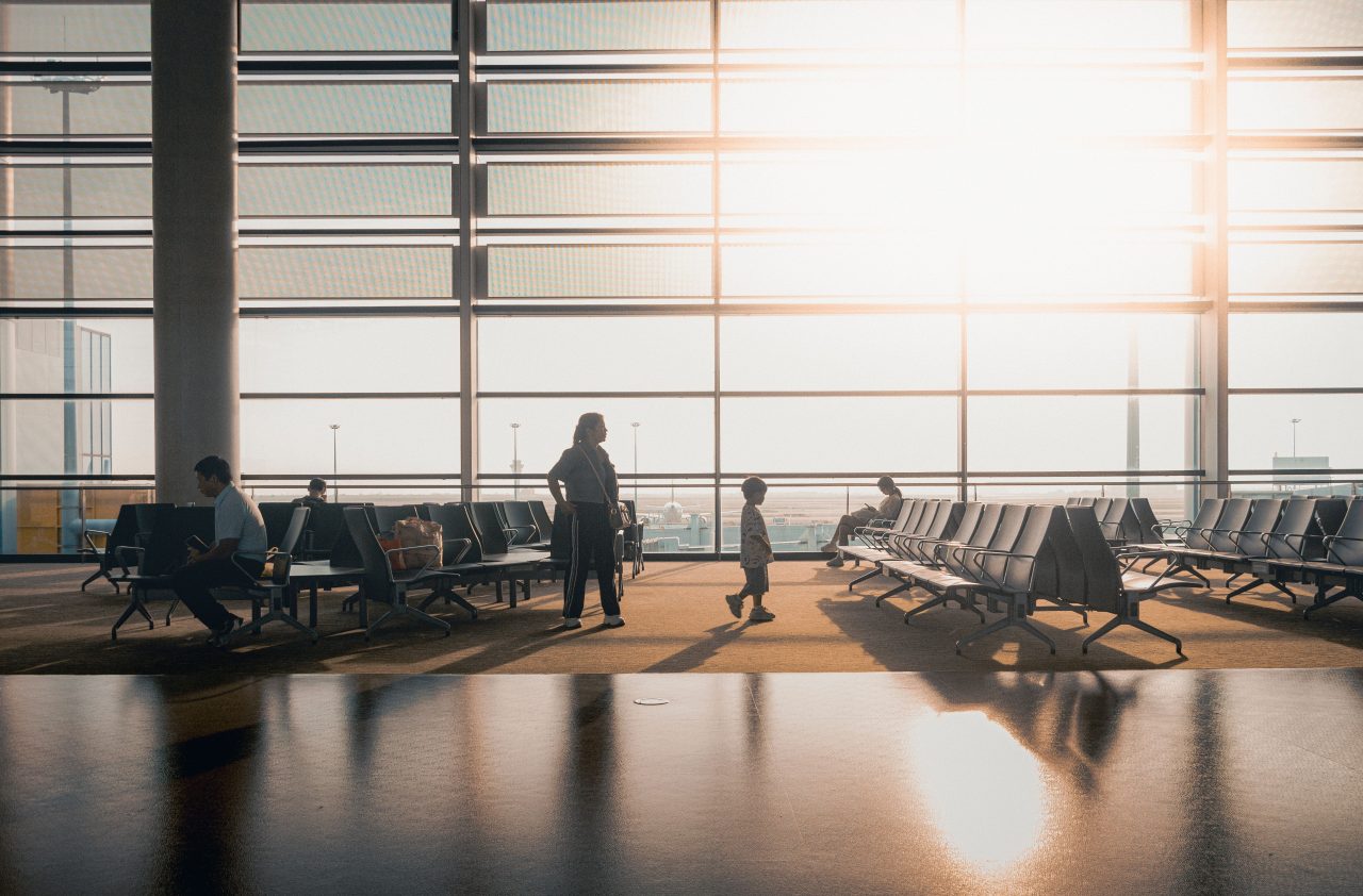 Travellers waiting in a sunlit airport departure lounge.